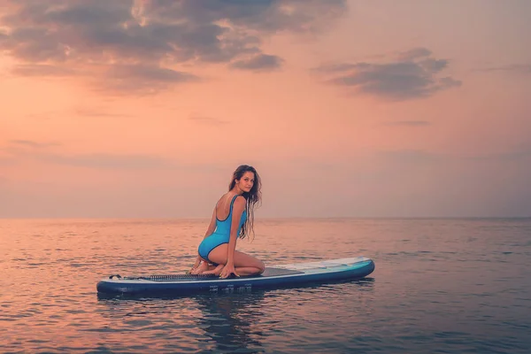 一个年轻性感的晒黑了的女人摆好姿势 坐在一个冲浪板上 后视镜夕阳西下复制空间 体育和冲浪的概念 — 图库照片