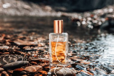 Erkekler güzel kokar. Nehir kıyısında duran dikdörtgen cam parfüm şişesi. Parfüm ve seçici parfüm konsepti.