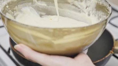 Kadın elinde hamurla bir kase tutuyor kaşıkla kızgın tavaya yağ döküyor. Yakın plan. Kahvaltıda ev yapımı krep pişiriyorum.