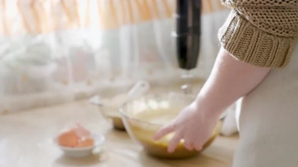 女性がミキサーでガラスボウルにパイ生地をホイップ テーブルの上には卵殻付きのプレートと小麦粉のボウルがあります バックビュー ジブが撃たれた 自家製ケーキを作るというコンセプト — ストック動画