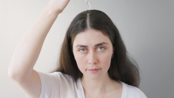 El retrato de la mujer caucásica que gotea el aceite cosmético sobre el cabello se separa y lo frota con los dedos. Fondo gris. El concepto de cuidado del cabello y alopecia. — Vídeos de Stock