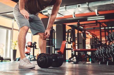 Sporcu adam spor salonunda dambıllarla antrenman yapıyor. Zindelik ve refah kavramı.