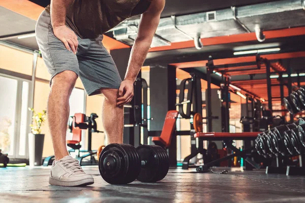 Sporcu adam spor salonunda dambıllarla antrenman yapıyor. Zindelik ve refah kavramı.