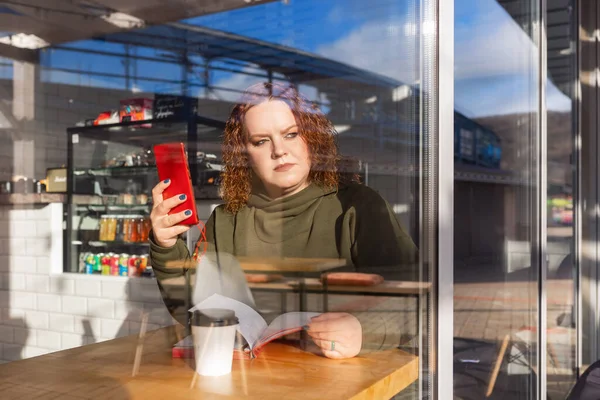 電話とノートを持つカフェに座っている特大のシリアス女性の肖像画 カフェの窓からは 二重露出をご覧ください ビジネスとフリーランスの概念 — ストック写真