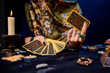 Falcı elinde bir kart fanatiği tutuyor Tarot ve bir kart gösteriyor. Yakın plan. Kehanet, sihir ve ezoterizm kavramı..