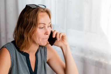 Uzaktan kumanda. Kadın evde bilgisayarın başında çalışıyor ve telefonla konuşuyor. Karantina, serbest çalışma ve kendini izole etme kavramı..