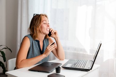 Uzaktan kumanda. Bir kadın evde grafik tabletle çalışıyor ve telefonda rahat bir şekilde konuşuyor. Karantina, serbest çalışma ve kendini izole etme kavramı..