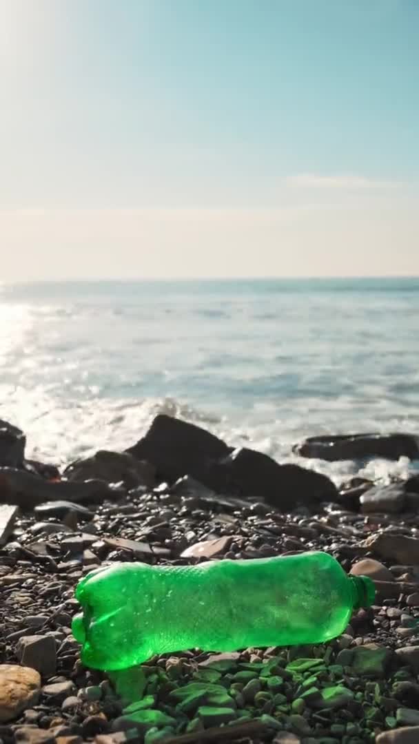 一个戴着橡胶手套的志愿者拿起一个塑料瓶 背景是海上冲浪 垂直方向 清理海岸和生态的概念 — 图库视频影像