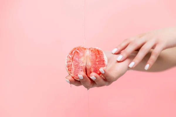 Woman\'s elegant hands hold half a grapefruit. Oil is poured on top of the fruit. Copy space. The concept of sexuality.