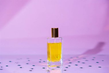 Transparent rectangular bottle of perfume on lilac background with drops. Perfumery and cosmetics. Copy space.
