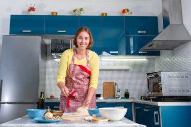 A young smiling woman in an apron kneads pizza dough. The concept of cooking homemade food and slow food.