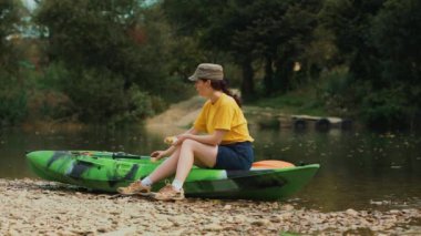 A young woman is sitting on a kayak and have a lunchtime. Real time. A boat floats in the background. The concept of outdoor activities and picnic