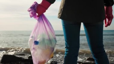 Dünya çevresi günü. Okyanus kıyısında bir gönüllü kadın plastik şişelerle dolu bir çöp torbası tutuyor. Çöp torbasını kapat. Okyanus ve ekolojinin temizlenmesi kavramı.