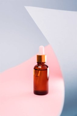 Close up of brown glass cosmetic bottle with dropper on a pink and gray background with abstract decor. The concept of an advertising template for beauty products.