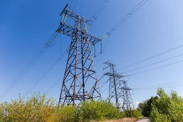 送電線の方向の場所で架空送電線の3つの鋼格子アンカー伝送塔は 空に対する低木に変化します — ストック写真