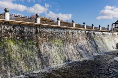 Nehirdeki beton baraj tarafından oluşturulan yapay şelale, parkın tepesindeki süslü metal çitlerle süslenmiş.