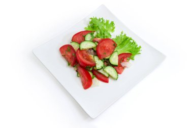 Dilimlenmiş taze domatesli sebze salatası, salatalık, marul ve doğranmış yeşillikler beyaz arka planda kare beyaz bir tabakta.