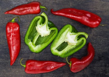 İki yarım taze yeşil dolma biber uzunlamasına kesilmiş koyu yüzey üzerinde kırmızı biber kabukları ile çevrili, üst manzara