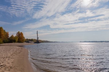 Sonbahar yapraklı ağaçlarla kaplı kumlu kıyısı olan geniş bir nehir, arka planda demirli yüzen bir vinç.