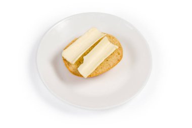 Küçük yuvarlak çöreğin yarısıyla yapılmış açık sandviç ve beyaz arka plandaki çay tabağının üzerinde iki ince dilim tereyağı var.