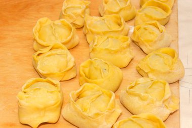 Türk mutfağında manti olarak bilinen ince hamur ambalajında baharatlı et karışımlı çiğ hamur köfteleri, ahşap kesme tahtasının üzerinde kaynamaya ya da buharlaşmaya hazırdır.