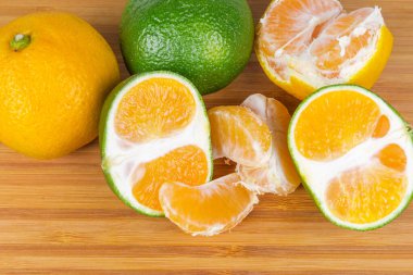 Olgun, sıradan mandalina ve mandalinaların hepsi ve yarısı yeşil kabuklu, ahşap bir yüzeye yakın çekim.