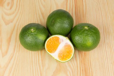 Olgun mandalinaların birkaçı, yeşil kabuklu, ahşap bir yüzeyin üst manzaralı.