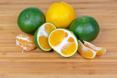 Olgun, sıradan mandalina ve mandalinaların bütün, yarımları ve segmentleri ahşap bir yüzey üzerinde yeşil kabuk ile çeşitlidir.