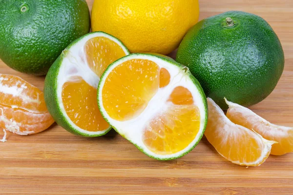 Olgun, sıradan mandalinalar ve mandalinaların bütün, yarım ve segmentleri yeşil kabuklu, ahşap bir yüzeye yakın çekim