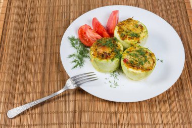 Pişmiş doldurulmuş sebze iliği parçaları ve bambu masa paspasında çatalla beyaz tabakta taze domates dilimleri.