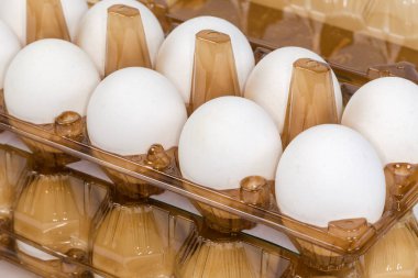 White chicken eggs in brown plastic transparent disposable egg packaging trays, fragment close-up in selective focus