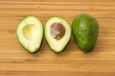 One whole and one halved pear-shaped avocado fruits with green skin, top view on a wooden surface