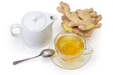 Çay kaşığı ve beyaz porselen çaydanlıkla cam bardakta zencefil çayı beyaz bir yüzey üzerinde taze zencefil köklerine karşı.
