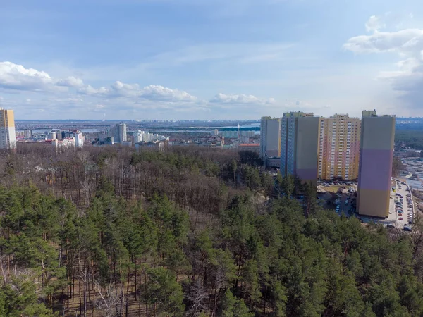 春の初春の晴れた日を背景に複数階建ての建物を持つ町の郊外の混合松や落葉樹林のセクション 航空ビュー — ストック写真