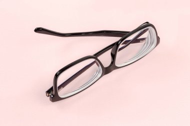 Siyah plastik çerçeveli modern klasik erkek gözlükleri. Pembe bir yüzey üzerinde kısmen katlanmış tapınakları var.