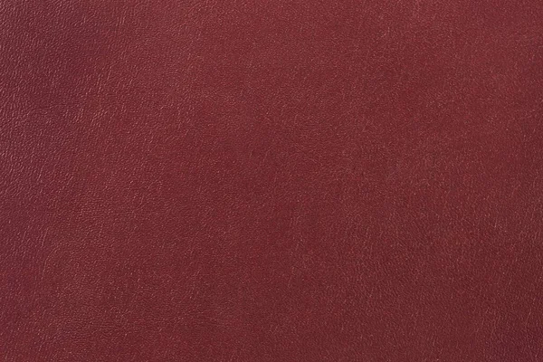 Fragment of the dark red hard cover of the book made with a fabric basis and plastic coating imitating leather close-up, texture, background