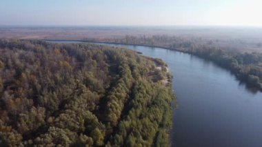 Sel çayırlarının arasındaki ağaçlarla kaplı nehir kıvrımları, hava manzarası.