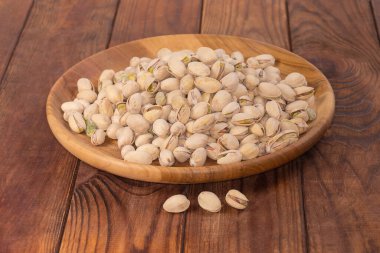 Bir yığın kavrulmuş tuzlu şam fıstığı kısmen açık kabuklu eski kırsal masada ahşap bir tabak, seçici bir odak noktasında kenar görüş