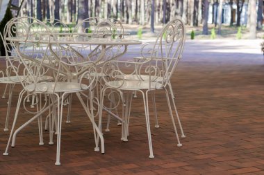 Beyaz, yuvarlak, metalik masalar ve yaz kafeteryasında kahverengi fayanslardan yapılmış, üstü açık sandalyeler.