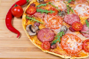 Ahşap kesim tahtasının üzerinde salam, sosis, domates ve mantardan yapılmış fırınlanmış pizzanın bir parçası.