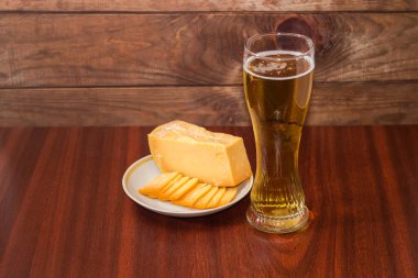 Bir bardak bira, bir parça ve ahşap masadaki tabakta birkaç ince dilim sert peynir.