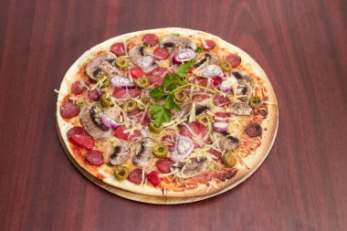 Farklı sebzelerle yuvarlak vejetaryen pizza ve kırmızı ahşap bir masada karton bir standın üzerinde düğme mantarlar.