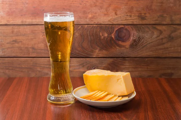 Bir bardak bira, bir parça ve ahşap masadaki tabakta birkaç ince dilim sert peynir.