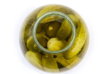 Büyük cam kavanozda baharatlı konserve salatalıklar, beyaz arka planda üst manzara.