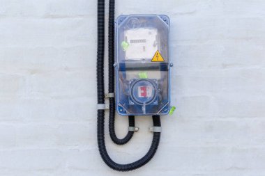 Dışarıdaki duvar beyazlatıcısının üzerine yerleştirilmiş özel şeffaf plastik kutuda fitil bulunan yerel dijital elektrik sayacı ve elektrik şalteri.