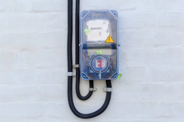 Domestic digital electricity meter and electrical switch with fuse in special transparent plastic case mounted on the brick whitewashed wall outdoor