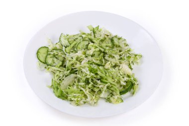 Dilimlenmiş taze lahana, salatalık, doğranmış soğan ve dereottan yapılmış yeşil baharatlı sebze salatası beyaz arka planda beyaz bir tabakta.