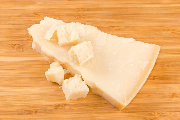 一块扁平的硬奶酪 以分段形式出现 在木制表面上有几块小碎块 — 图库照片