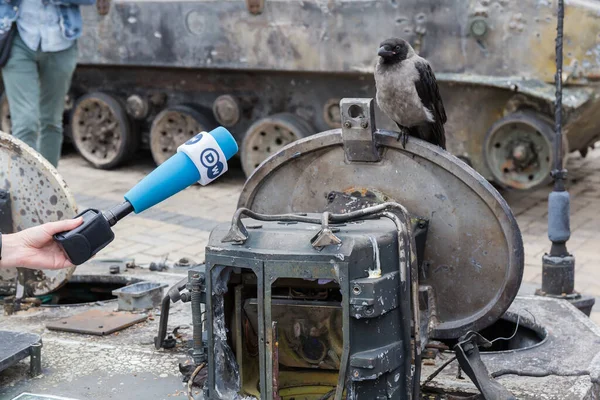Kyiv Ukraine 2022年6月23日 ロシアのウクライナ侵攻で破壊されたロシアの軍事機器の博覧会 破壊された戦闘車両のハッチに街のカラスと彼女の前でマイクと手 — ストック写真