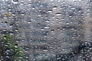 Wet car windshield covered with water flowing streams and drops different sizes during a rain, inside view in selective focus